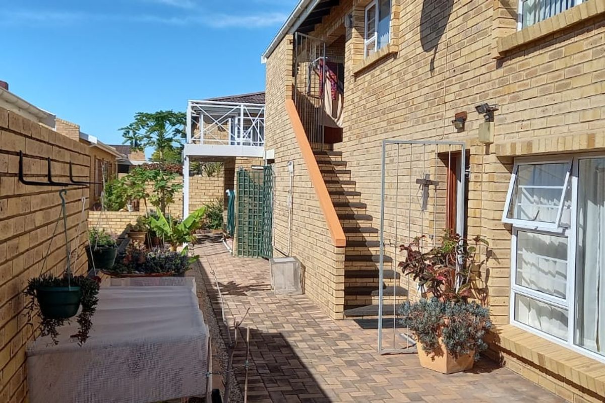 Exterior view of a retirement village unit featuring face-brick construction, paved walkways, external staircase, and security gates.
