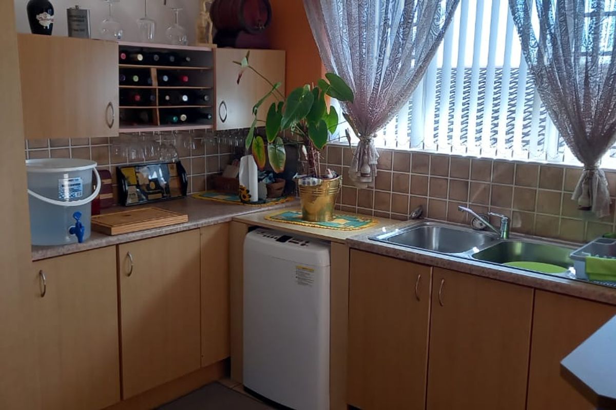 A functional kitchen area featuring light wood-toned cabinetry, tiled splashbacks, and a double-basin stainless steel sink with a window view.