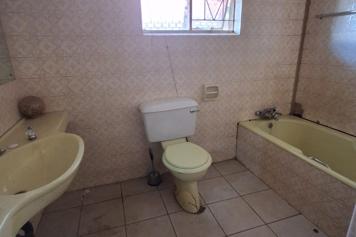 A dated bathroom featuring original pastel-colored sanitary ware, including a bathtub, pedestal basin, and toilet, with floor-to-ceiling wall tiles.
