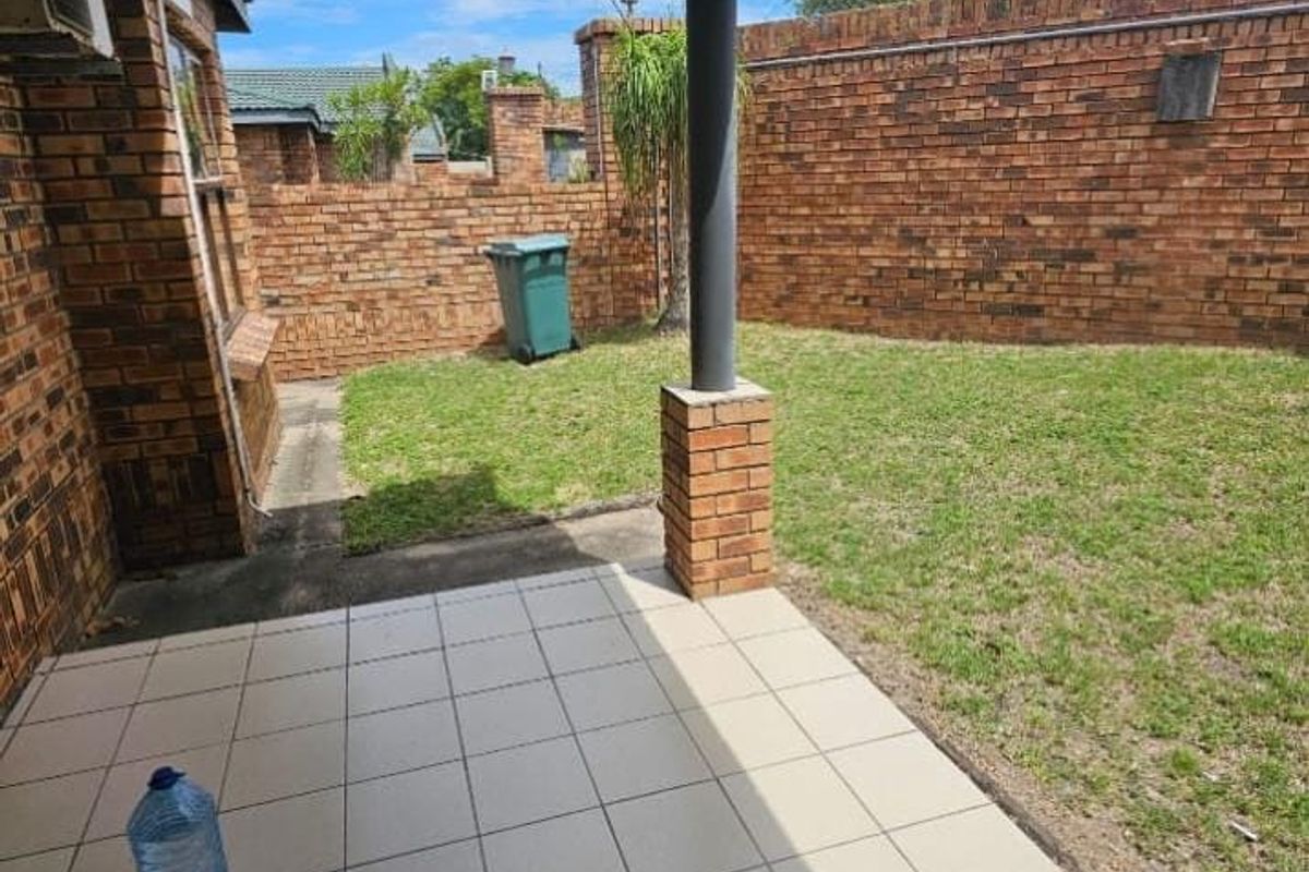 A private rear garden featuring a tiled patio area, brick boundary walls, and a small lawn space.