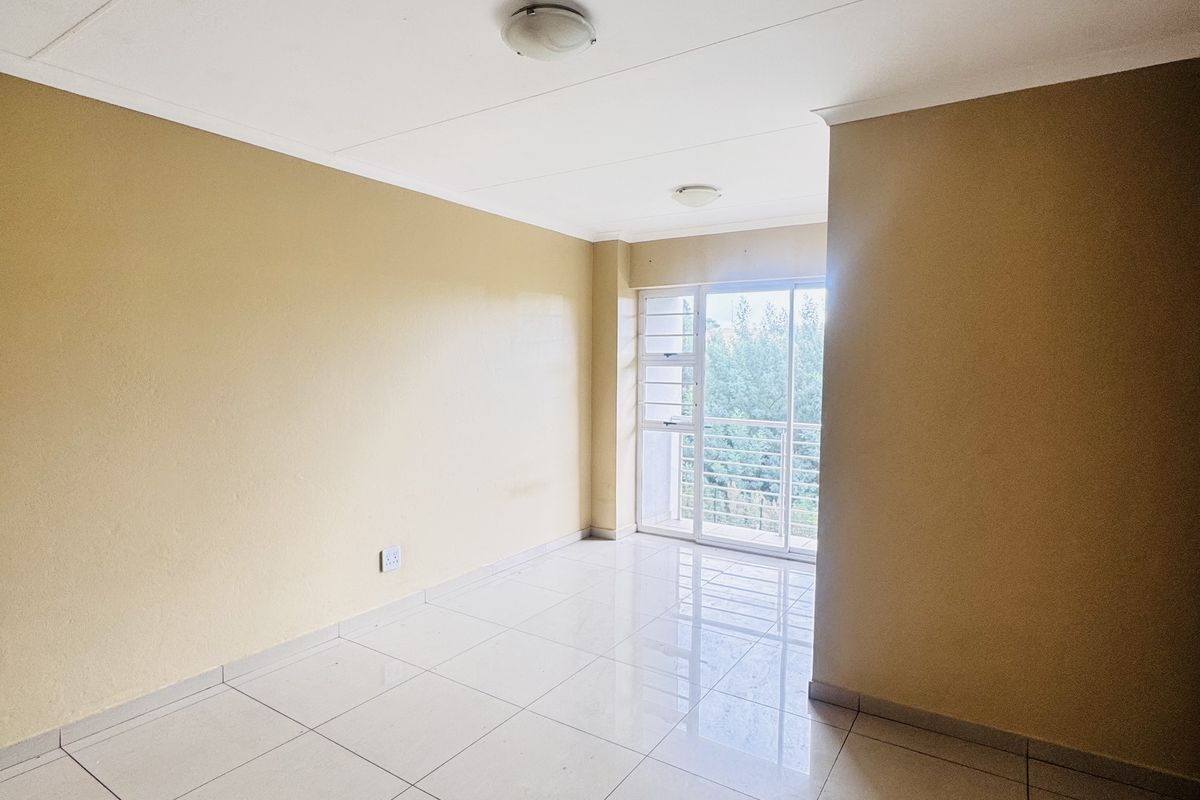A bright, empty living area featuring neutral wall tones, polished ceramic floor tiles, and a sliding glass door leading to an outdoor balcony.
