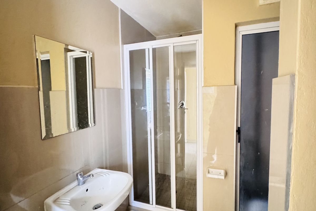 A functional bathroom featuring a pedestal basin, a glass-enclosed shower, and a standard toilet, finished with neutral wall and floor tiling.