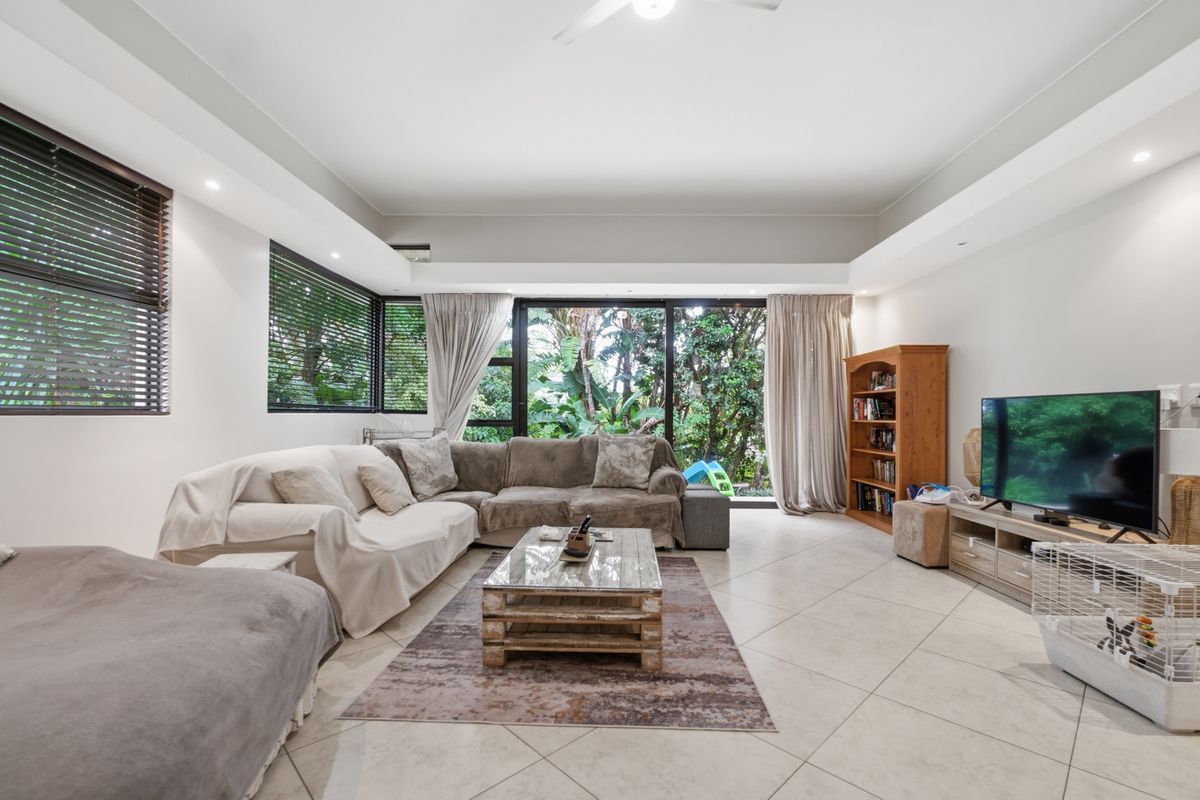 Spacious living room featuring large sliding glass doors that open to a lush garden view, complemented by tiled flooring and recessed ceiling lighting.