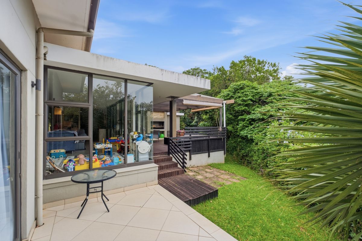 A spacious rear patio featuring tiled flooring, timber decking, and a built-in outdoor fireplace, overlooking a private garden area.