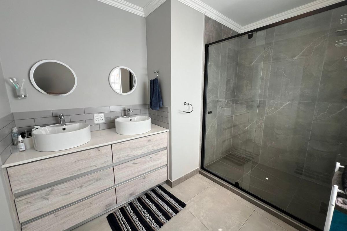 Modern bathroom featuring a double vanity with vessel sinks, stone-look floor tiles, and a spacious walk-in shower with a black-framed glass enclosure.