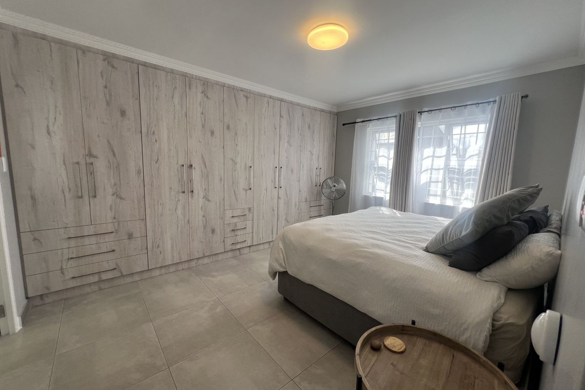 A well-maintained bedroom featuring extensive built-in cabinetry with a wood-grain finish, large format floor tiles, and crown molding.