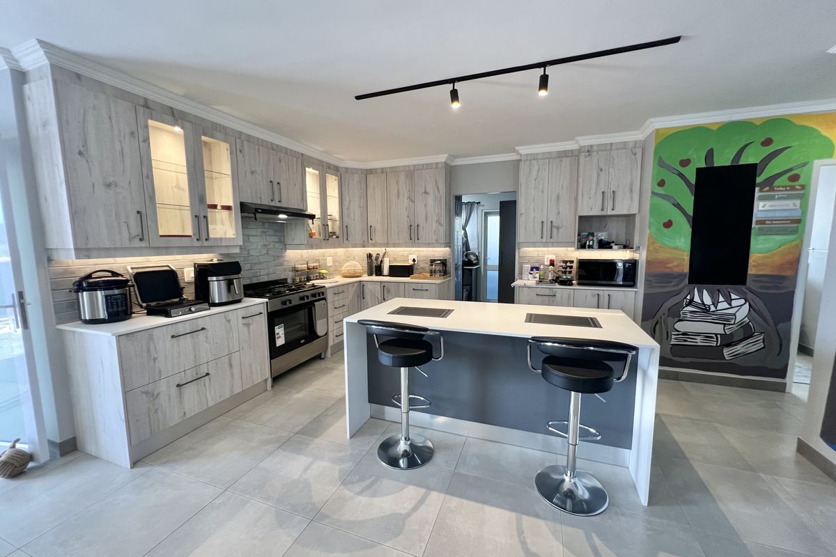 Modern kitchen featuring light wood-grain cabinetry, a central island with breakfast bar seating, integrated lighting, and tiled flooring.
