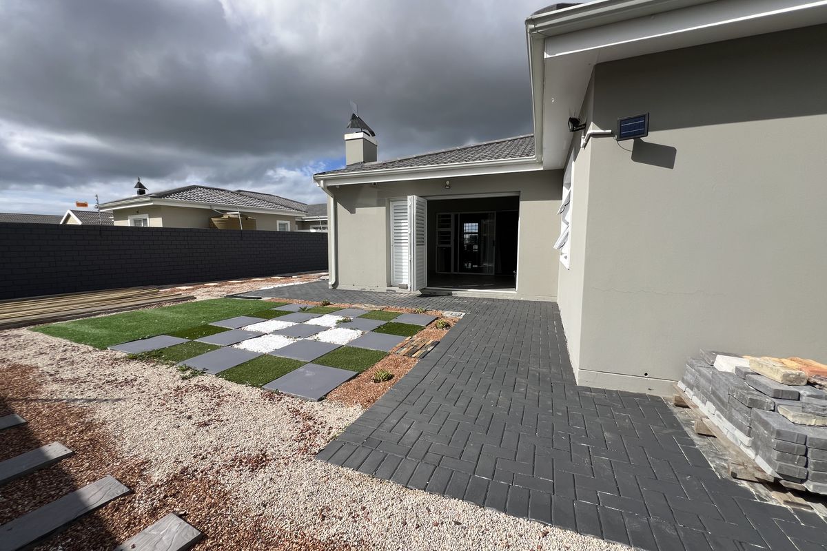Rear exterior view featuring a paved patio area, landscaped garden sections with artificial turf and stone, and direct access to the interior living space.