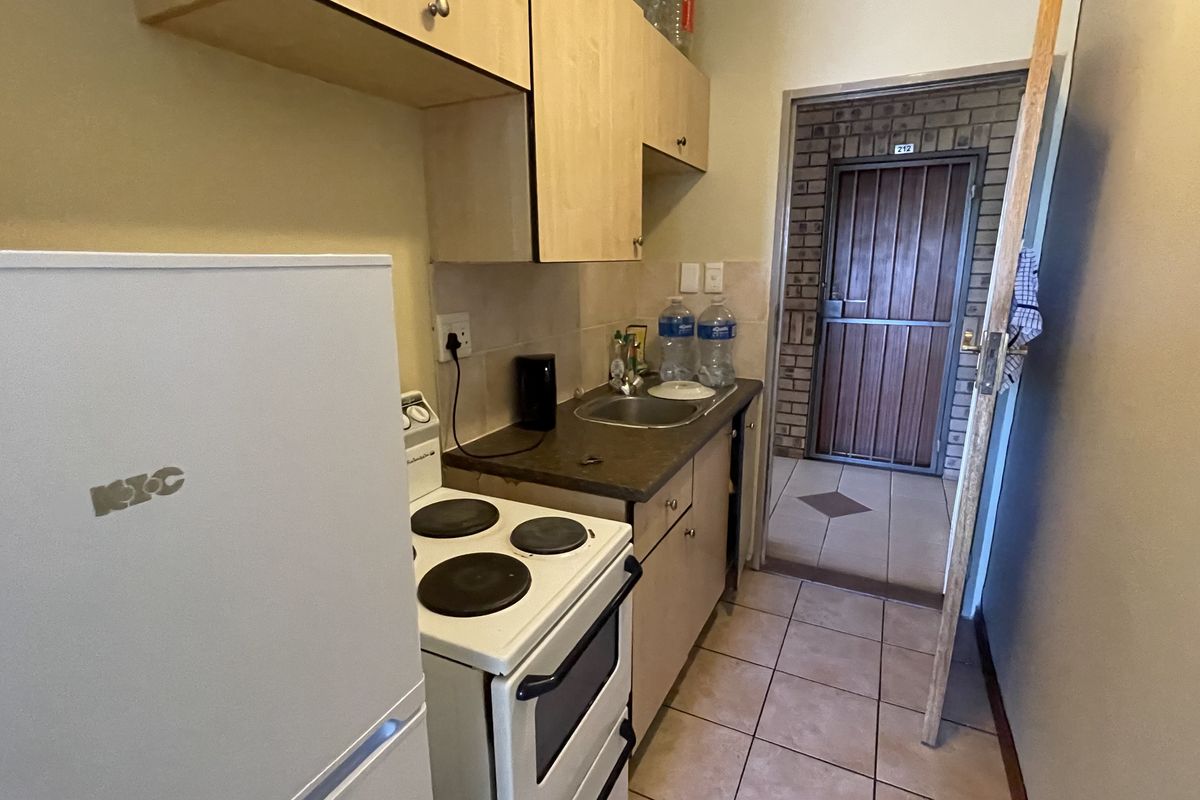 Compact kitchen area featuring laminate cabinetry, a built-in sink, and a freestanding electric stove, leading directly to the apartment entrance.