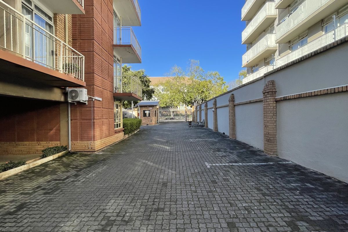 A paved driveway area between apartment buildings, featuring a perimeter boundary wall and access to a gated entrance.