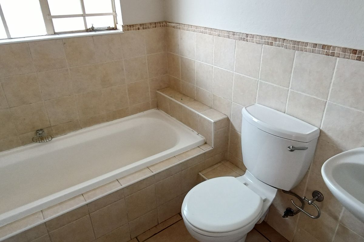 A functional bathroom featuring a built-in bathtub, pedestal basin, and toilet with neutral wall tiling and a decorative mosaic border.