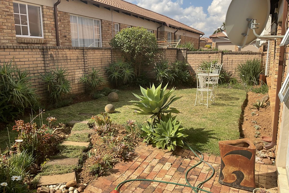 A private rear garden featuring a brick-paved patio area, established lawn, perimeter brick walling, and mature succulent landscaping.