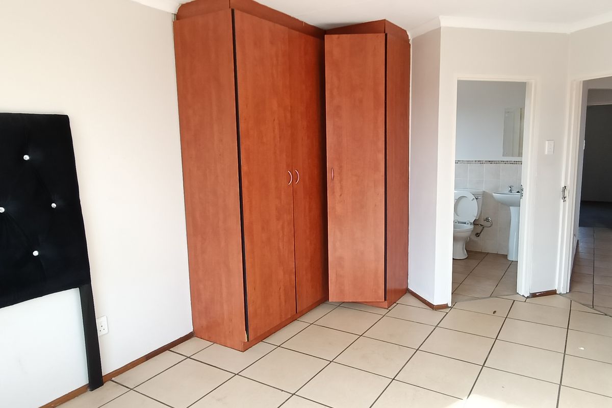 Bedroom featuring built-in wooden cupboards and an en-suite bathroom with tiled flooring throughout.