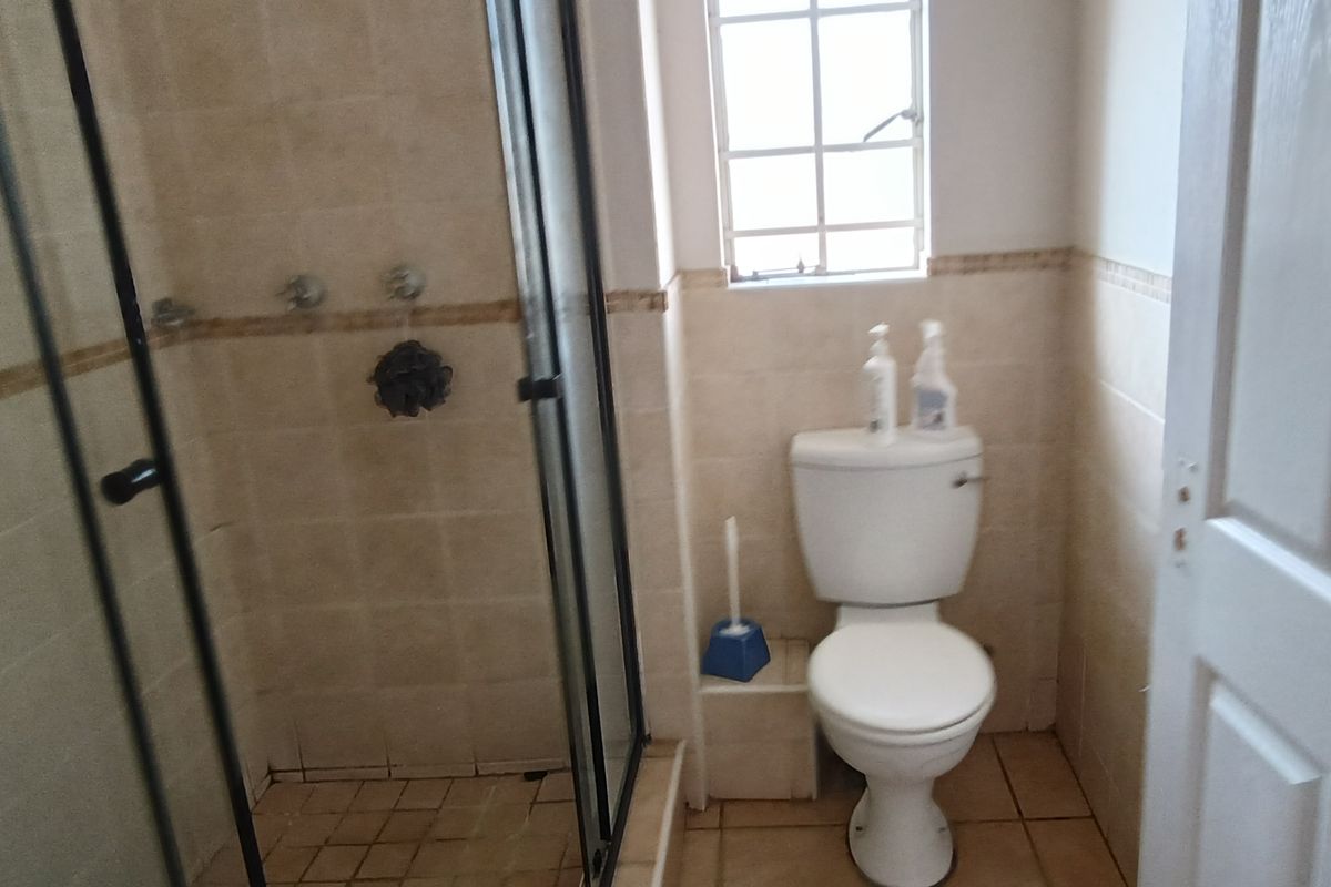 A functional bathroom featuring a glass-enclosed shower and a standard toilet, finished with neutral wall and floor tiling.