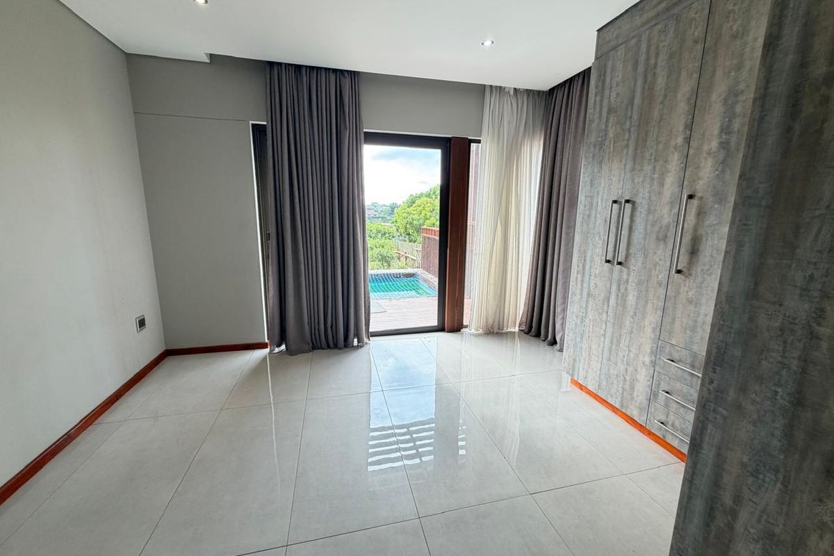 A bright bedroom featuring large format floor tiles, built-in cupboards with a textured finish, and sliding glass doors opening to a pool deck.