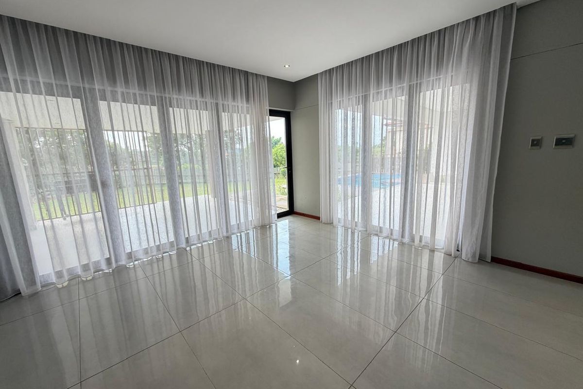 Spacious living area featuring large glass sliding doors with sheer curtains, polished tile flooring, and direct access to the outdoor patio and pool area.