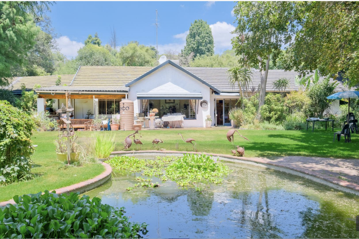 Rear view of the house featuring a well-maintained garden, a decorative pond, and a covered patio area attached to the main building structure.