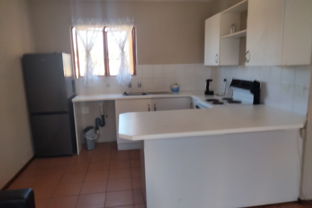 A functional kitchen featuring built-in cabinetry, a tiled splashback, a breakfast bar, and an electric stove, with tiled flooring throughout.
