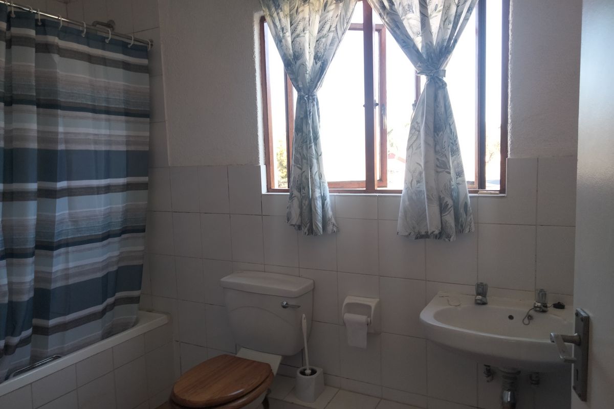 A dated bathroom featuring a bathtub with shower, wall-mounted basin, and toilet, requiring cosmetic updates to modernize the space.