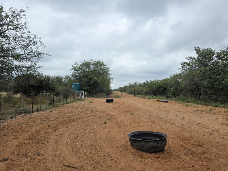 A view of the farm landscape featuring a dirt access track, perimeter wire fencing, and a water storage tank.