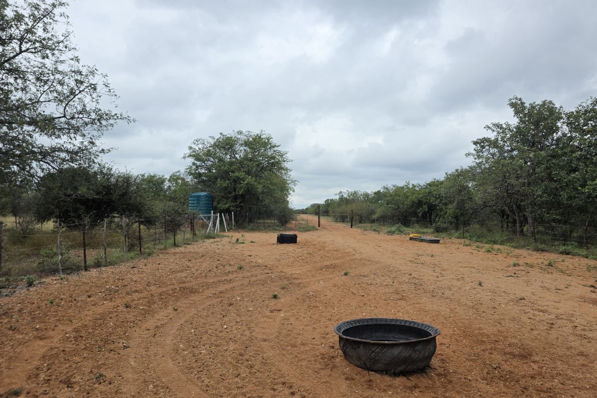 A view of the farm landscape featuring a dirt access track, perimeter wire fencing, and a water storage tank.
