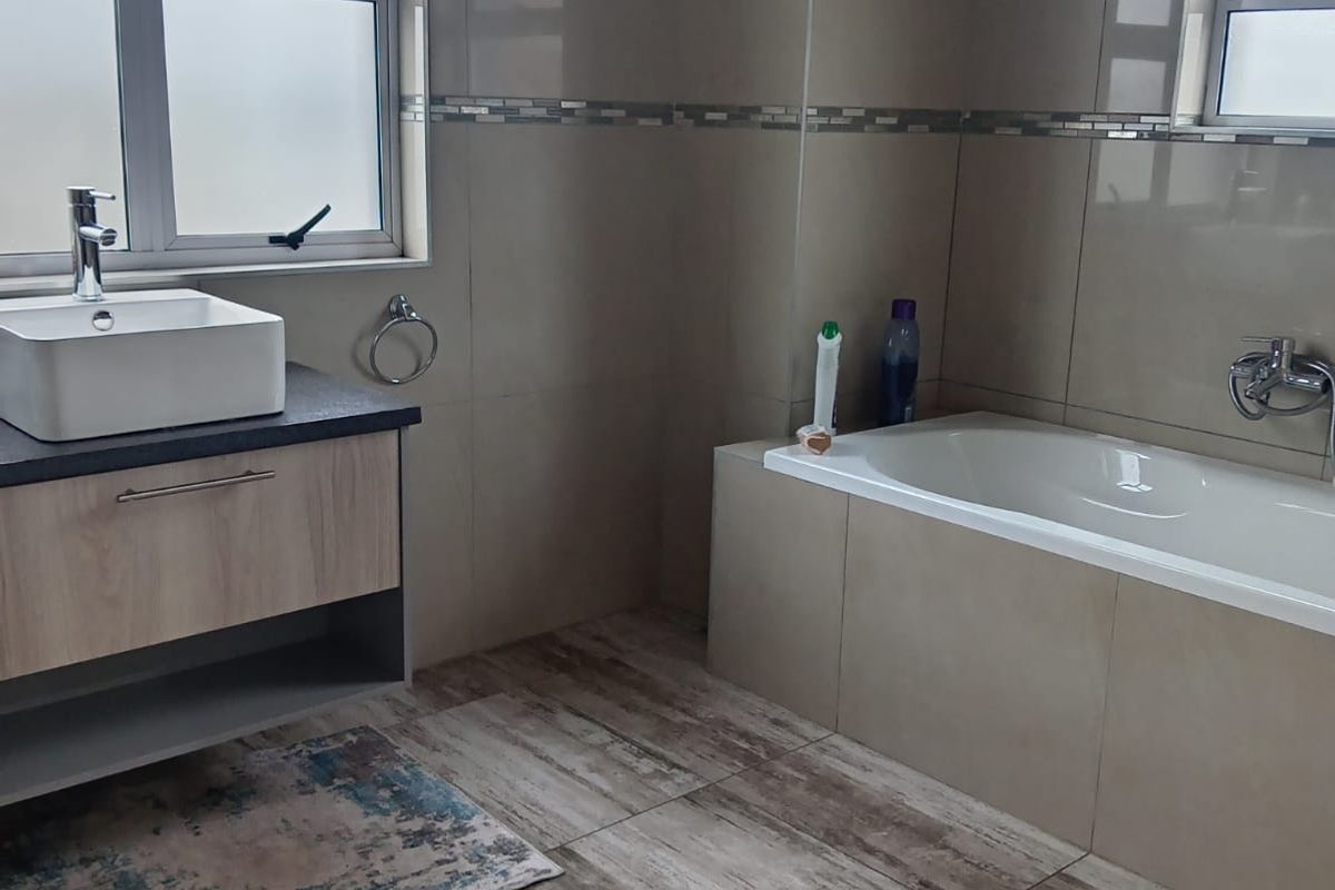 Modern bathroom featuring a floating vanity with a vessel sink, a built-in bathtub, and neutral floor-to-ceiling tiling.
