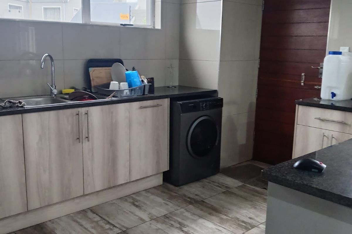 A functional kitchen featuring light wood-grain cabinetry, dark granite countertops, tiled flooring, and a built-in space for a washing machine.