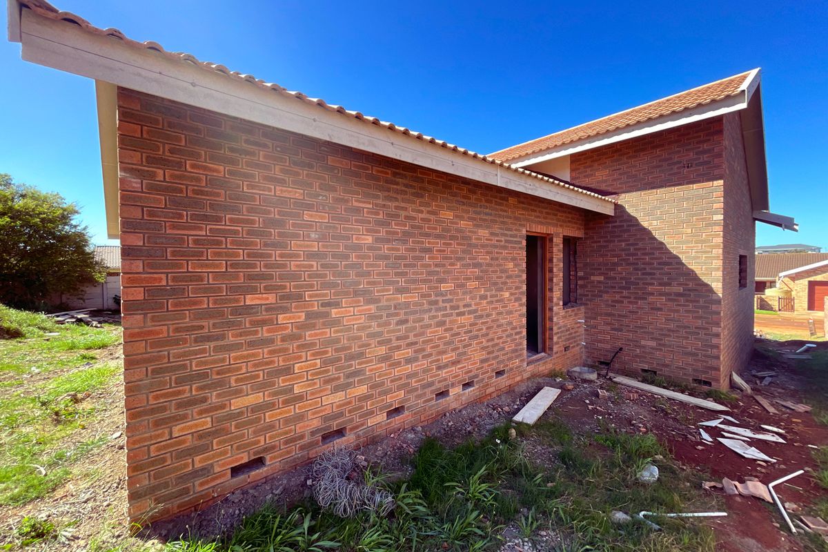 Exterior view of a brick house under construction, featuring a tiled roof and unfinished surrounding grounds.
