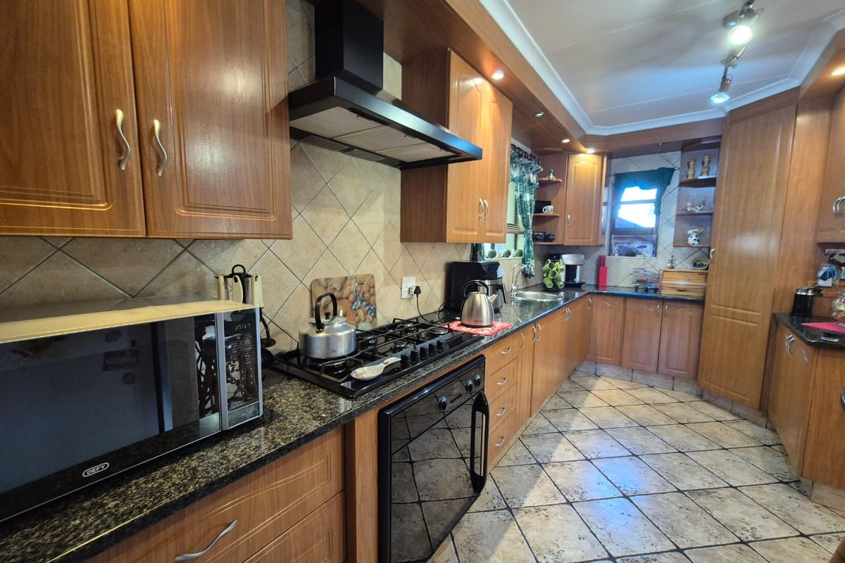 A functional kitchen featuring wood-finish cabinetry, granite countertops, a built-in gas hob, extractor fan, and tiled flooring.