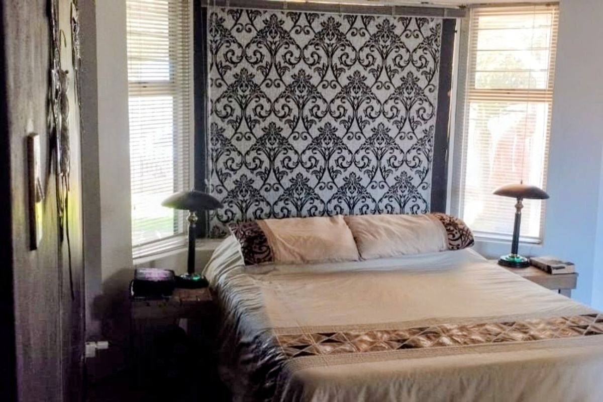 A bedroom featuring large windows with blinds, laminate flooring, and a decorative wall feature behind the bed area.