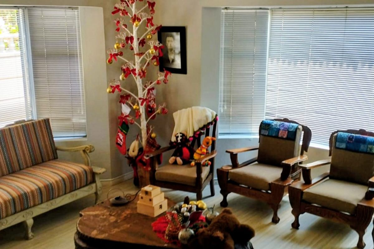 A bright living room featuring large bay windows with fitted horizontal blinds and light-toned flooring.