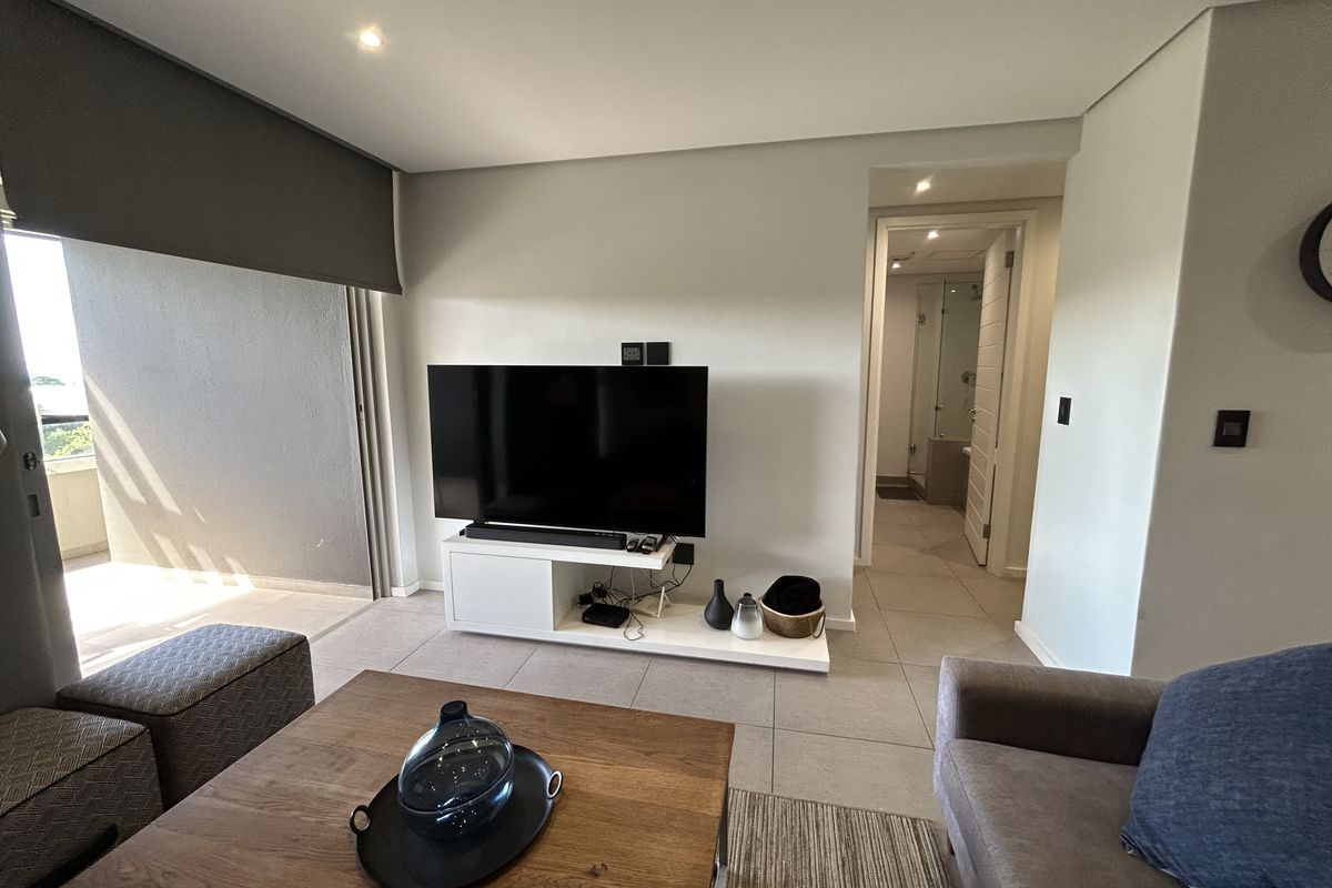 A modern living room featuring large sliding doors leading to a balcony, with neutral tiled flooring and recessed ceiling lighting.