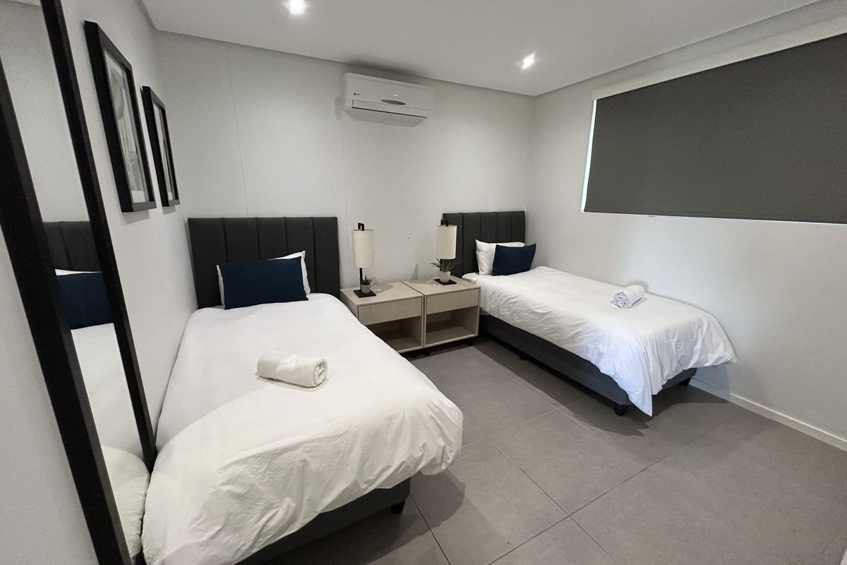 A modern, well-maintained bedroom featuring neutral floor tiles, recessed ceiling lighting, and a wall-mounted air conditioning unit.