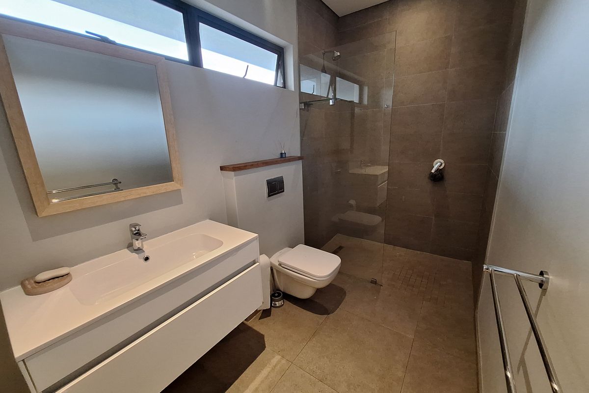 Modern bathroom featuring a wall-hung vanity, frameless glass shower enclosure, wall-mounted toilet, and large format floor-to-ceiling tiling.