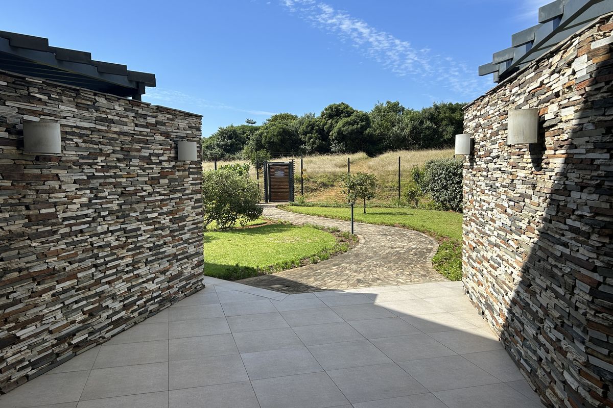 A well-maintained rear patio area featuring stacked stone walls, large format floor tiles, and a landscaped garden path leading to the perimeter fence.
