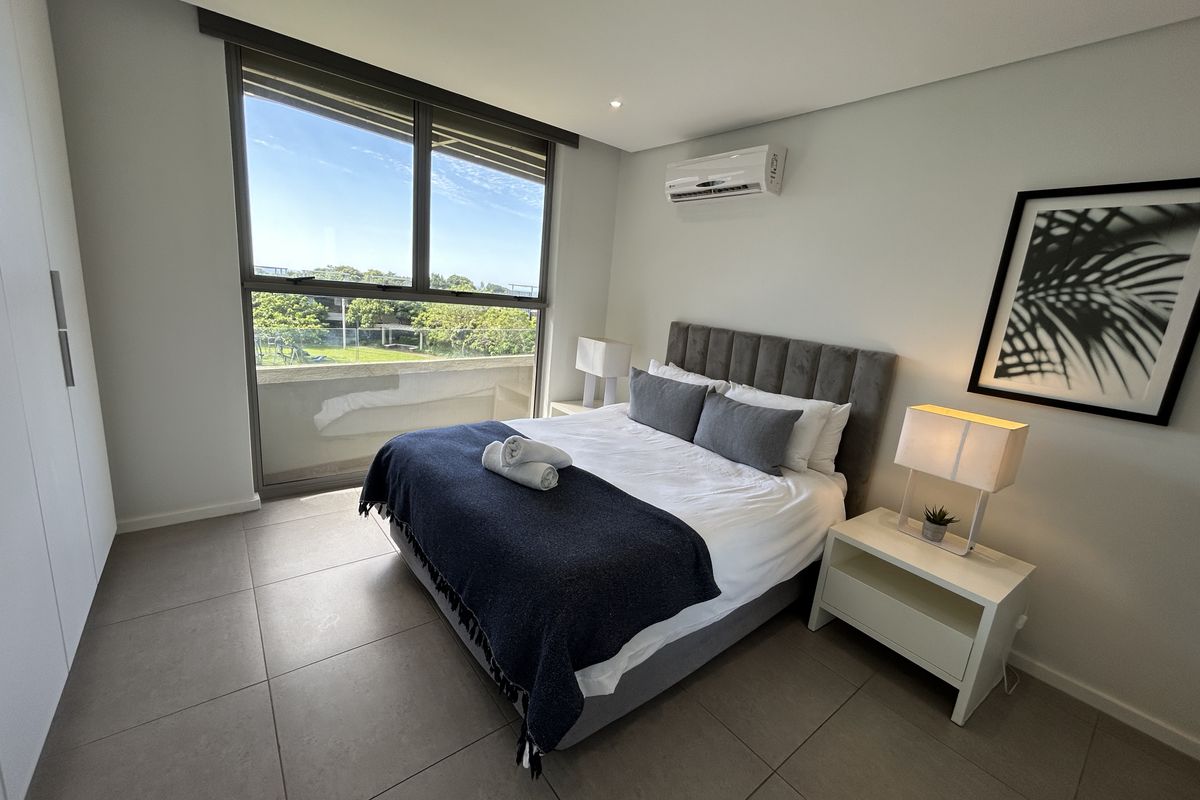 Modern bedroom featuring tiled floors, built-in cupboards, a split-system air conditioner, and large sliding glass doors leading to a balcony.