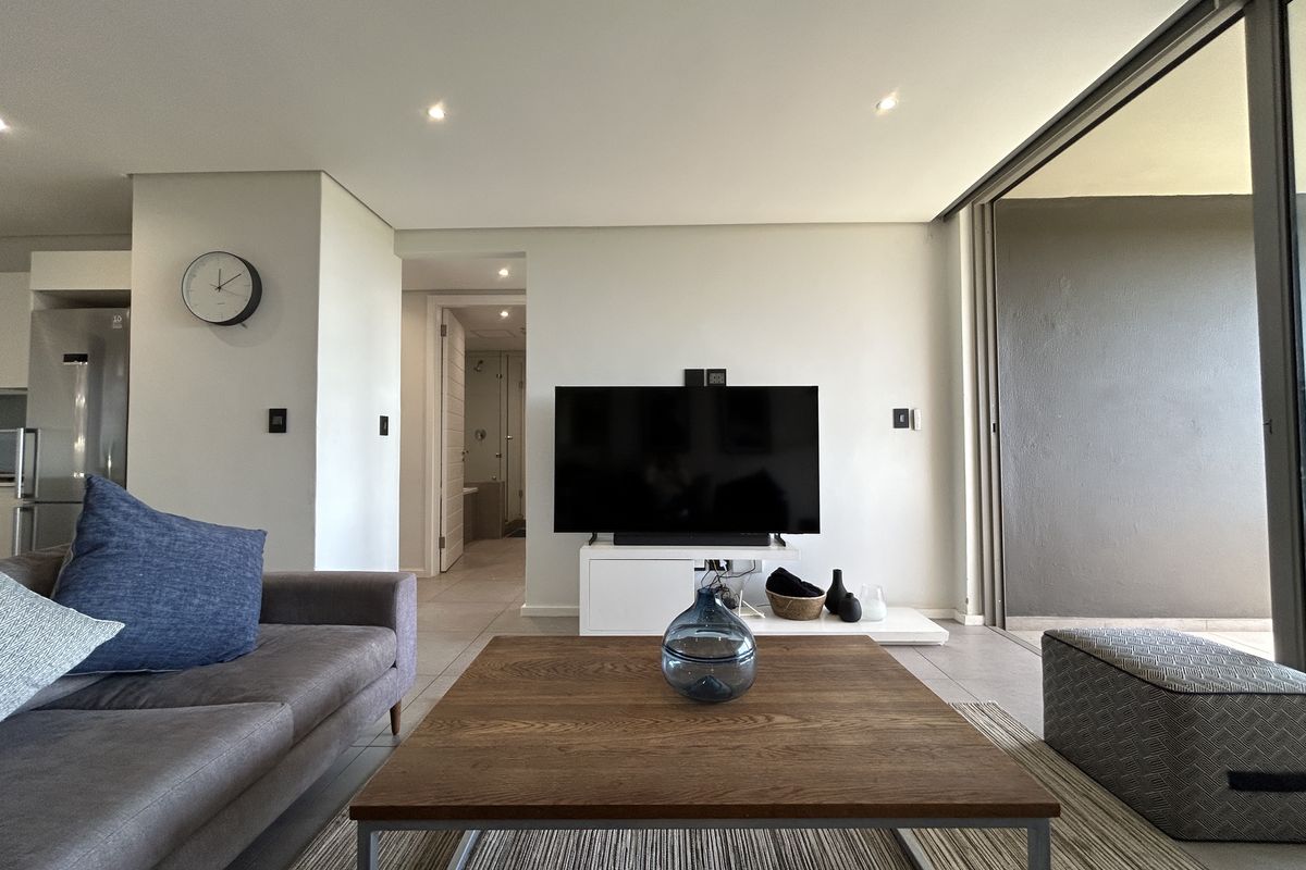 A modern, well-lit living room featuring tiled floors, recessed lighting, and large sliding glass doors that provide seamless access to the balcony.