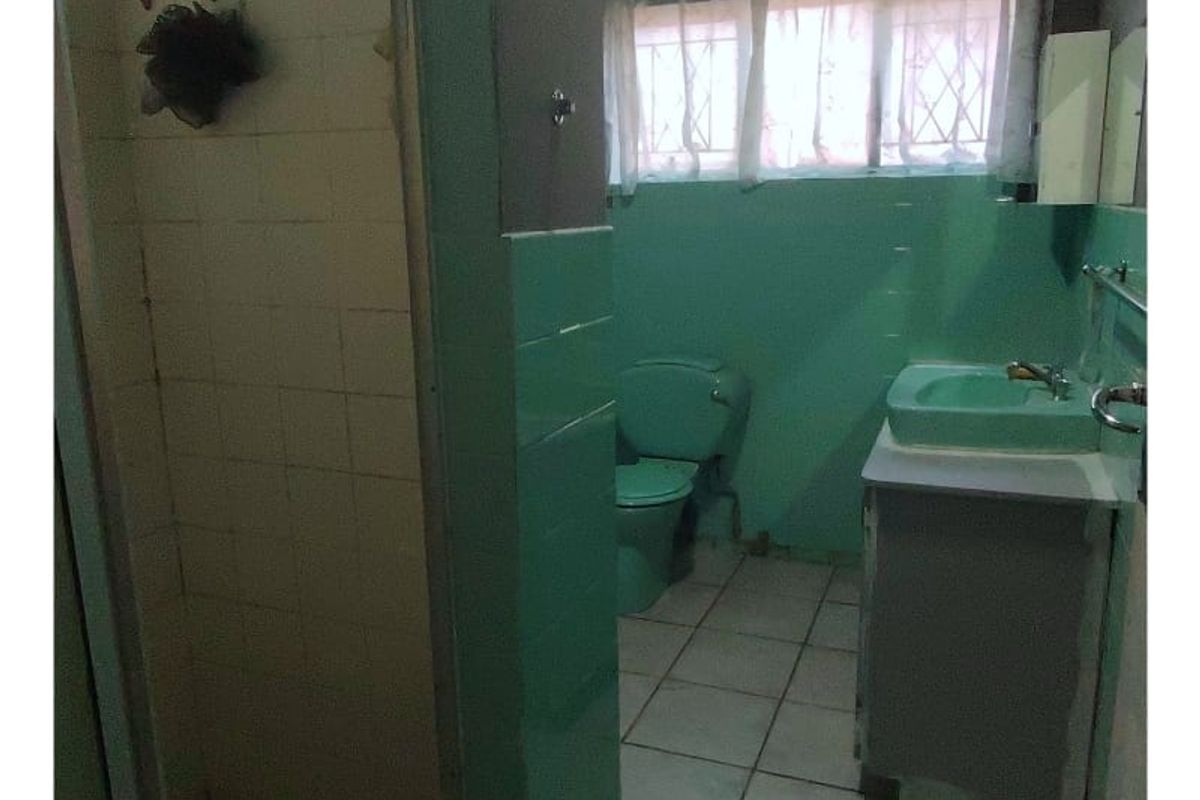 A dated bathroom featuring a walk-in shower, a mint green toilet, and a matching vanity basin with tiled flooring.