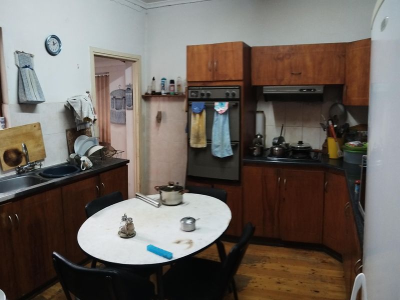 A dated kitchen featuring wooden cabinetry, built-in oven, extractor fan, and timber flooring, offering potential for a modern renovation.
