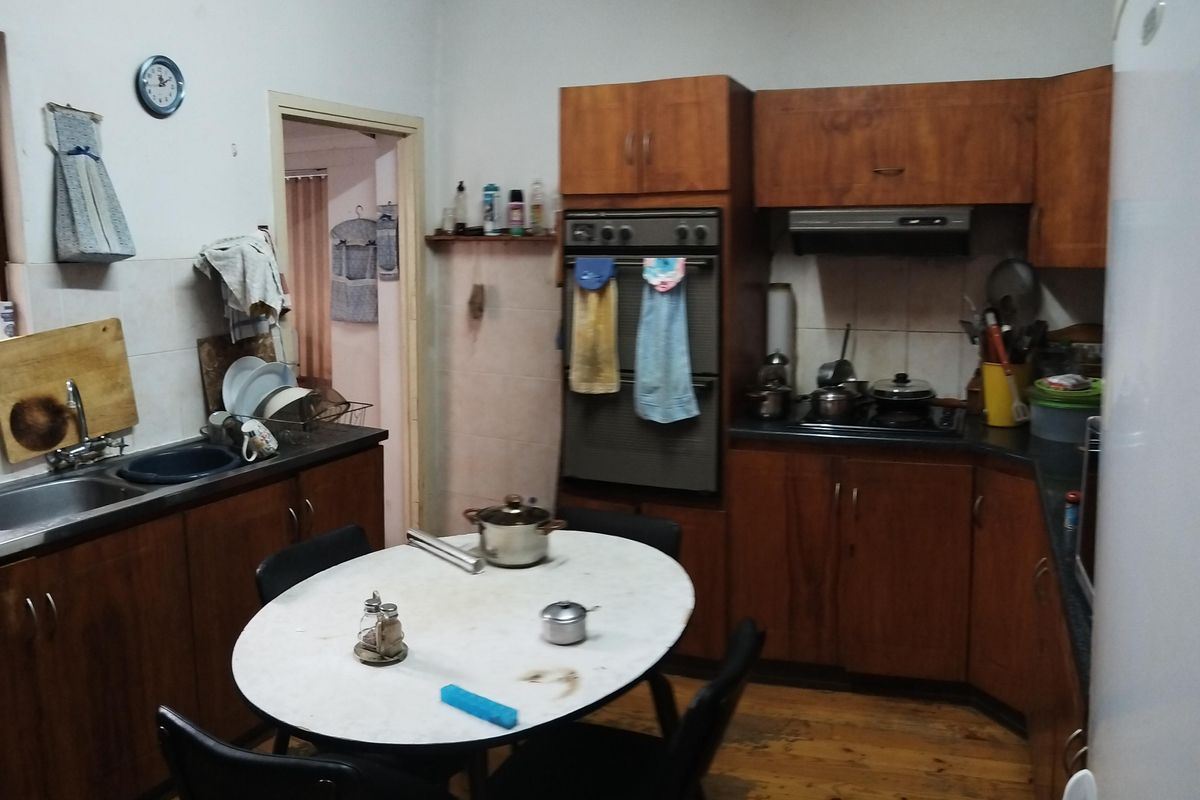 A dated kitchen featuring wooden cabinetry, built-in oven, extractor fan, and timber flooring, offering potential for a modern renovation.