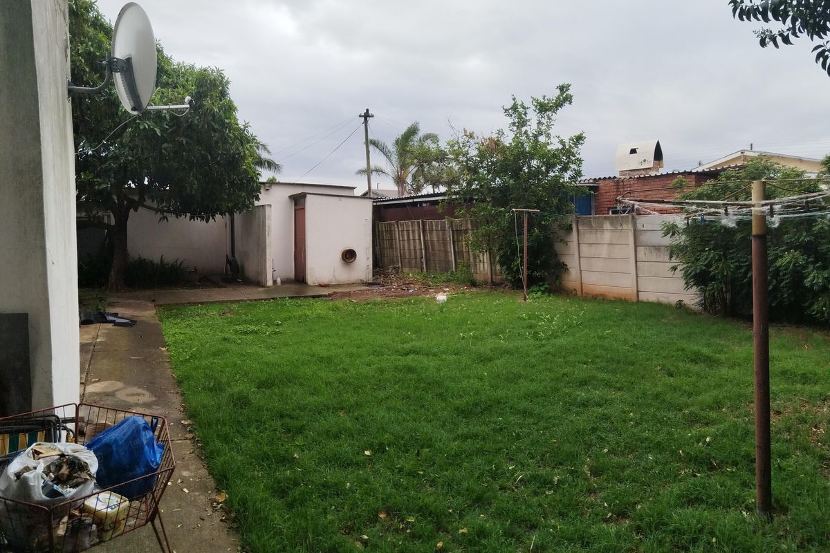 A rear garden area featuring a lawn, concrete boundary walls, paved walkway, and a fixed rotary clothesline.