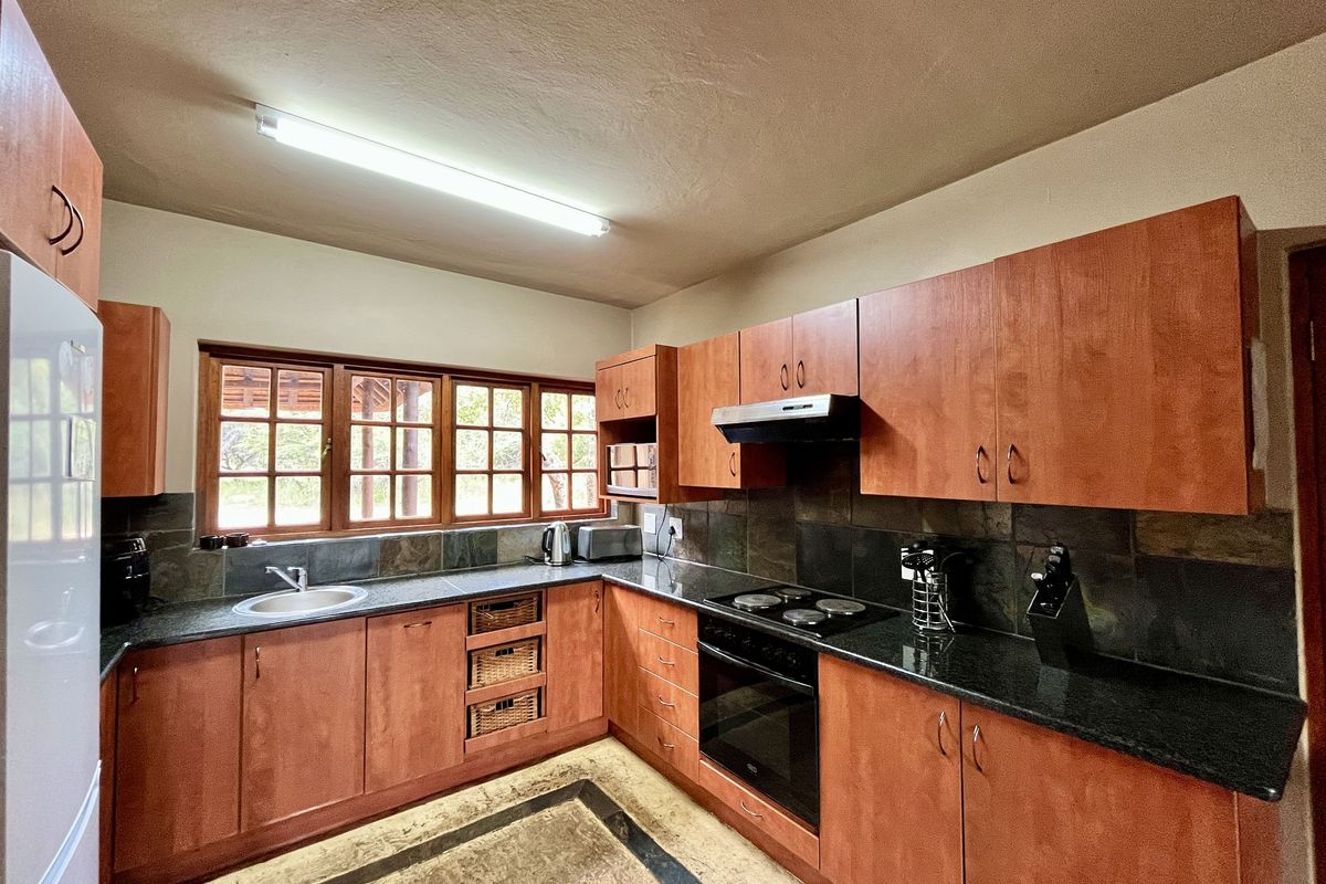 A functional kitchen featuring wooden cabinetry, dark granite countertops, a built-in oven with extractor fan, and a tiled backsplash with natural light.