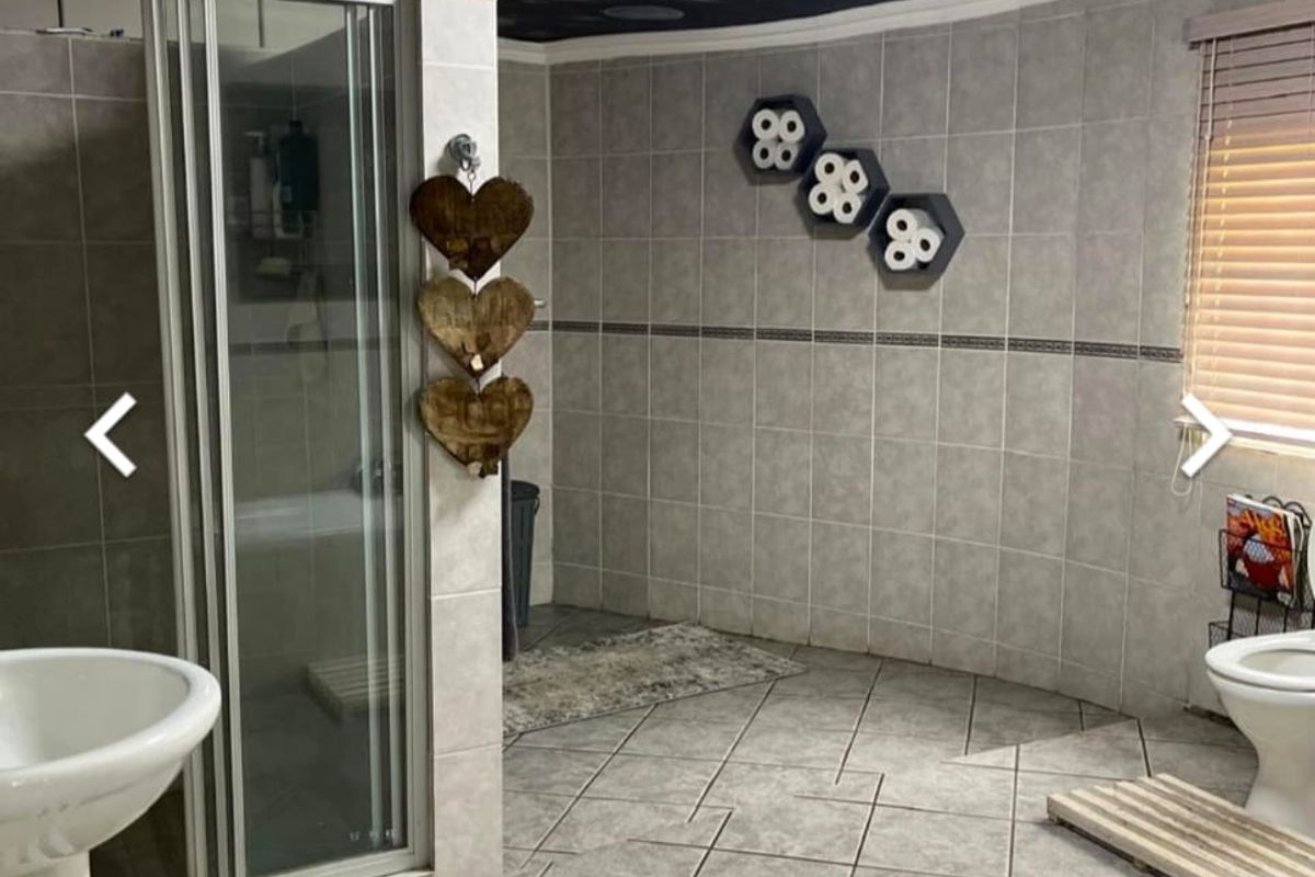 A spacious bathroom featuring a glass-enclosed shower, pedestal basin, and toilet, finished with neutral wall tiles and a unique dark ceiling treatment.