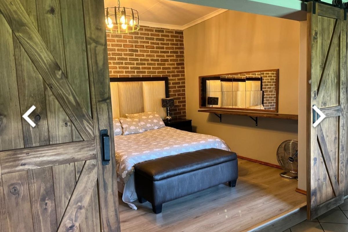 A cozy bedroom featuring a rustic brick accent wall, laminate flooring, and sliding barn-style wooden doors for a unique architectural touch.