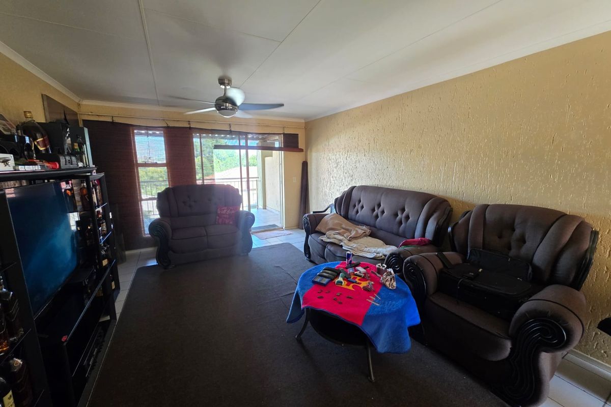 A spacious living room featuring tiled flooring, a ceiling fan, and sliding glass doors that open onto an attached balcony.
