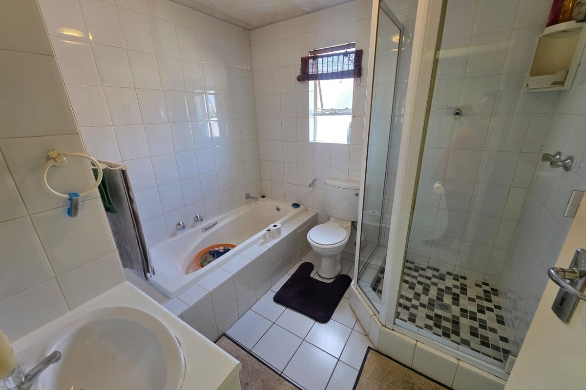A functional bathroom featuring a built-in bathtub, separate glass-enclosed shower, toilet, and vanity basin with tiled walls and flooring.