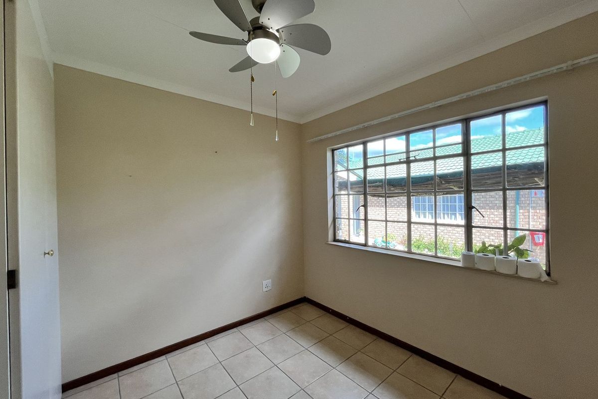 A bright, empty bedroom featuring tiled flooring, a ceiling fan, and a window with security bars, offering a clean canvas for personalization.