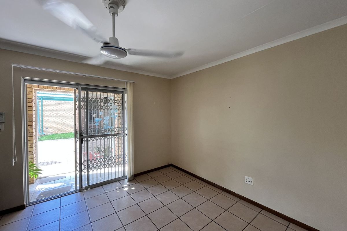 An empty living room featuring tiled flooring, a ceiling fan, and a sliding glass door providing access to an outdoor patio area.