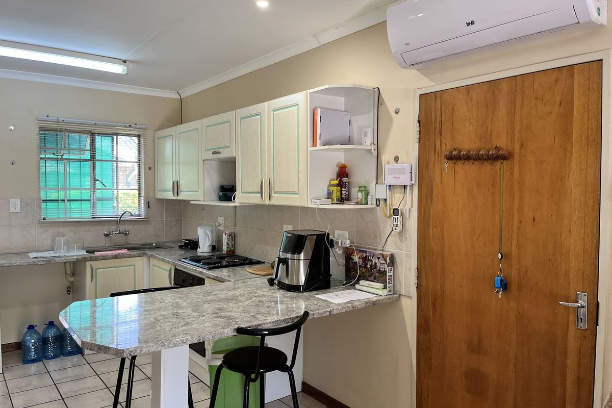 Functional kitchen featuring built-in cabinetry, laminate countertops, gas hob, tiled backsplash, and a wall-mounted air conditioning unit.