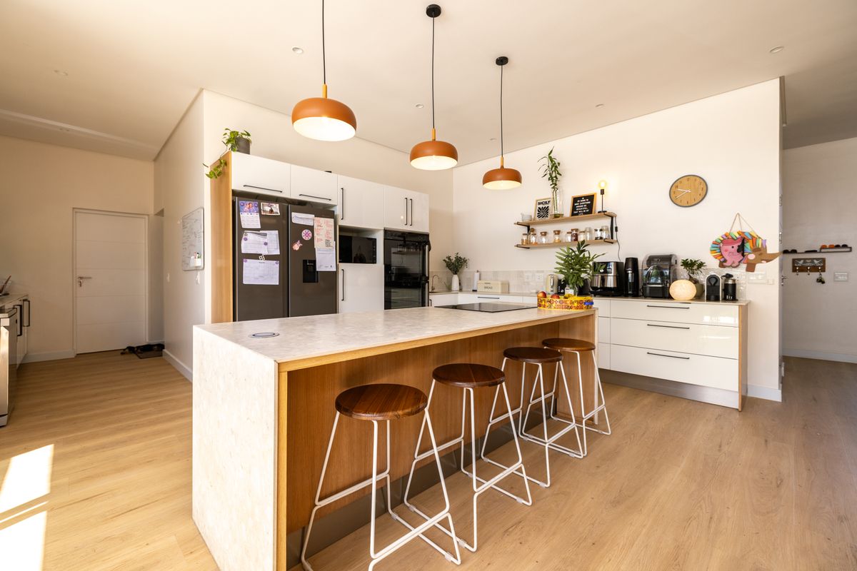 Modern kitchen featuring a central island with breakfast bar seating, sleek white cabinetry, integrated appliances, and warm timber-look flooring.